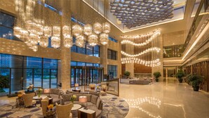 A spacious lobby with a high ceiling, large chandeliers, and a modern geometric ceiling design. - Hilton Urumqi (Ürümqi)