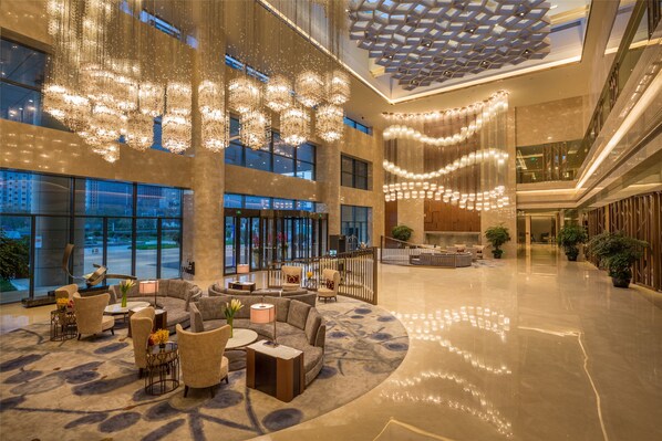 Un vestíbulo espacioso con techo alto, grandes candelabros y un diseño geométrico moderno.