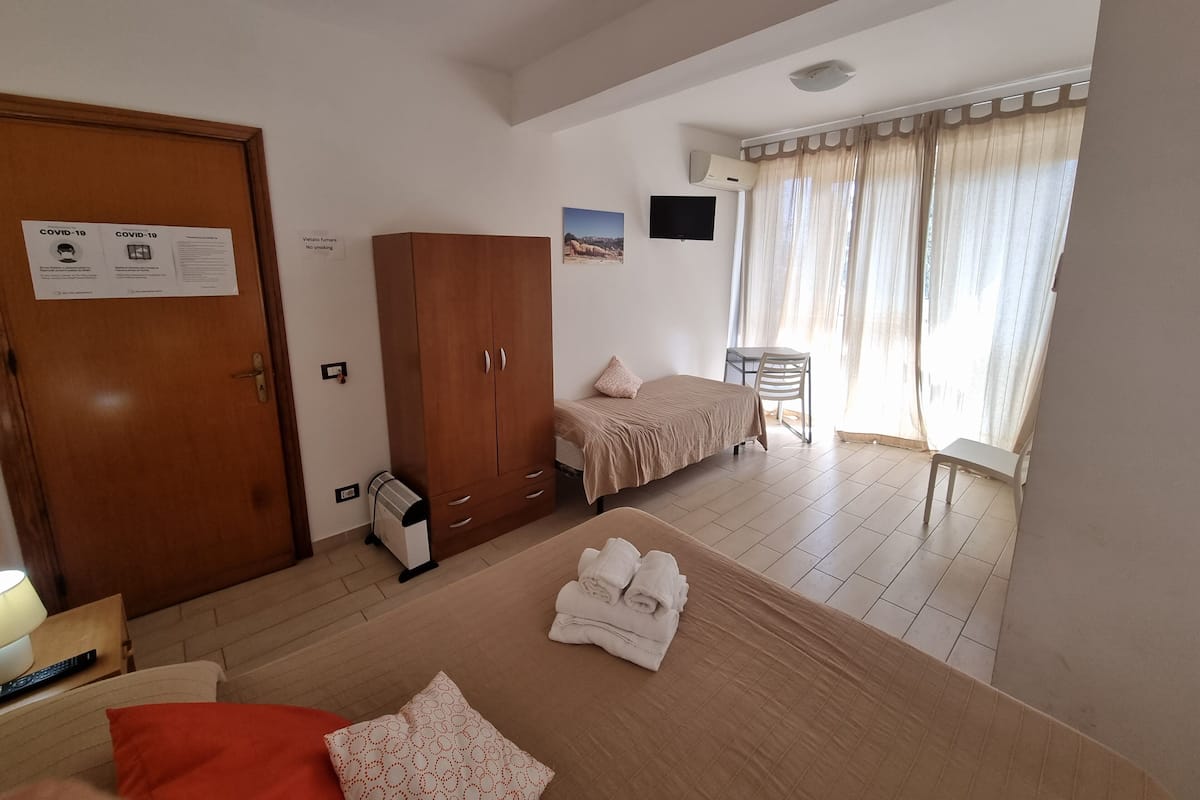 Een slaapkamer met een bed, een kledingkast, een bureau, een stoel en een televisie aan de muur.