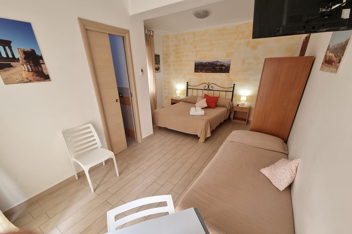 Een hotelkamer met een bed, een stoel, een kleine tafel en een aan de muur bevestigde televisie.