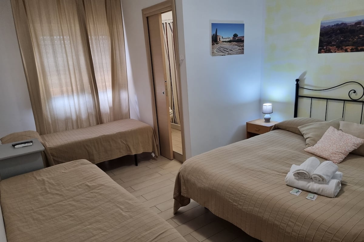 Een hotelkamer met twee enkele bedden, een nachtkastje met een lamp, een klein bureau met een afstandsbediening en een deur naar een badkamer.