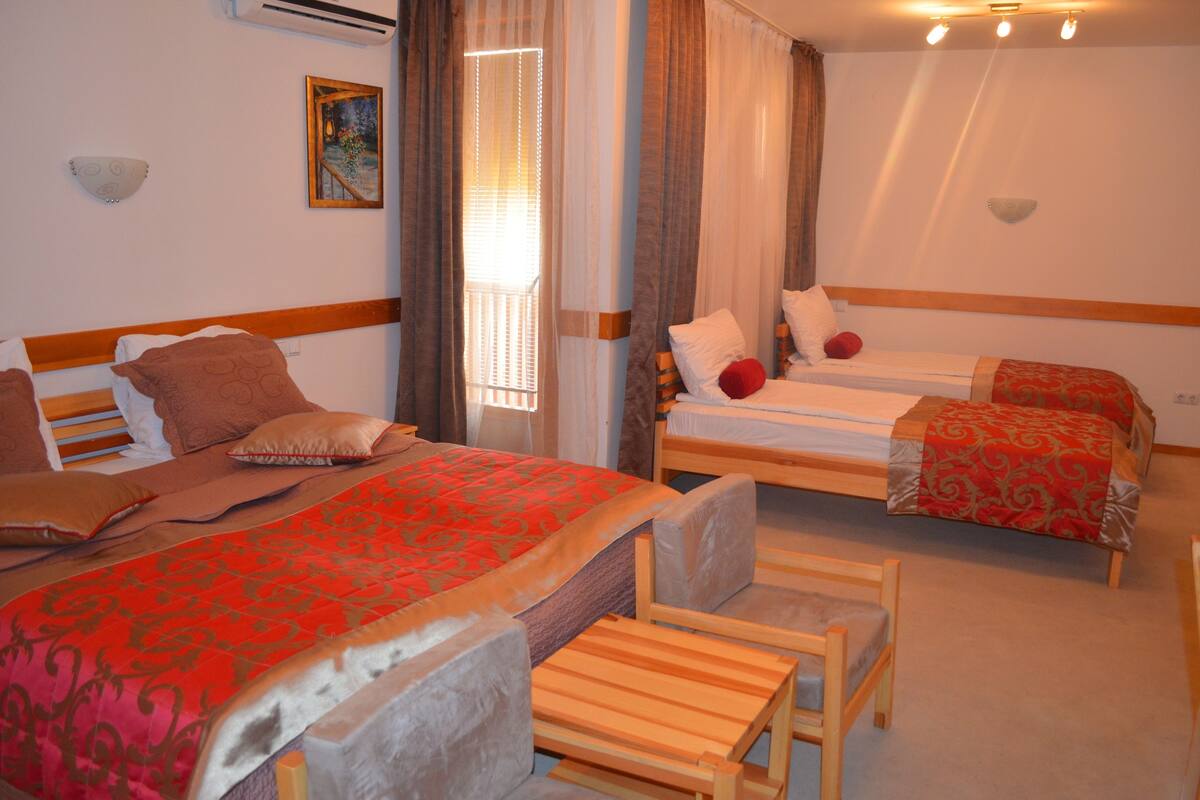 A hotel room with two single beds, a wooden headboard, a small wooden table, and a chair.