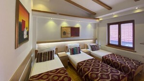 Une chambre d’hôtel avec quatre lits simples, des poutres en bois au plafond, une grande fenêtre avec des stores et un tableau au mur.