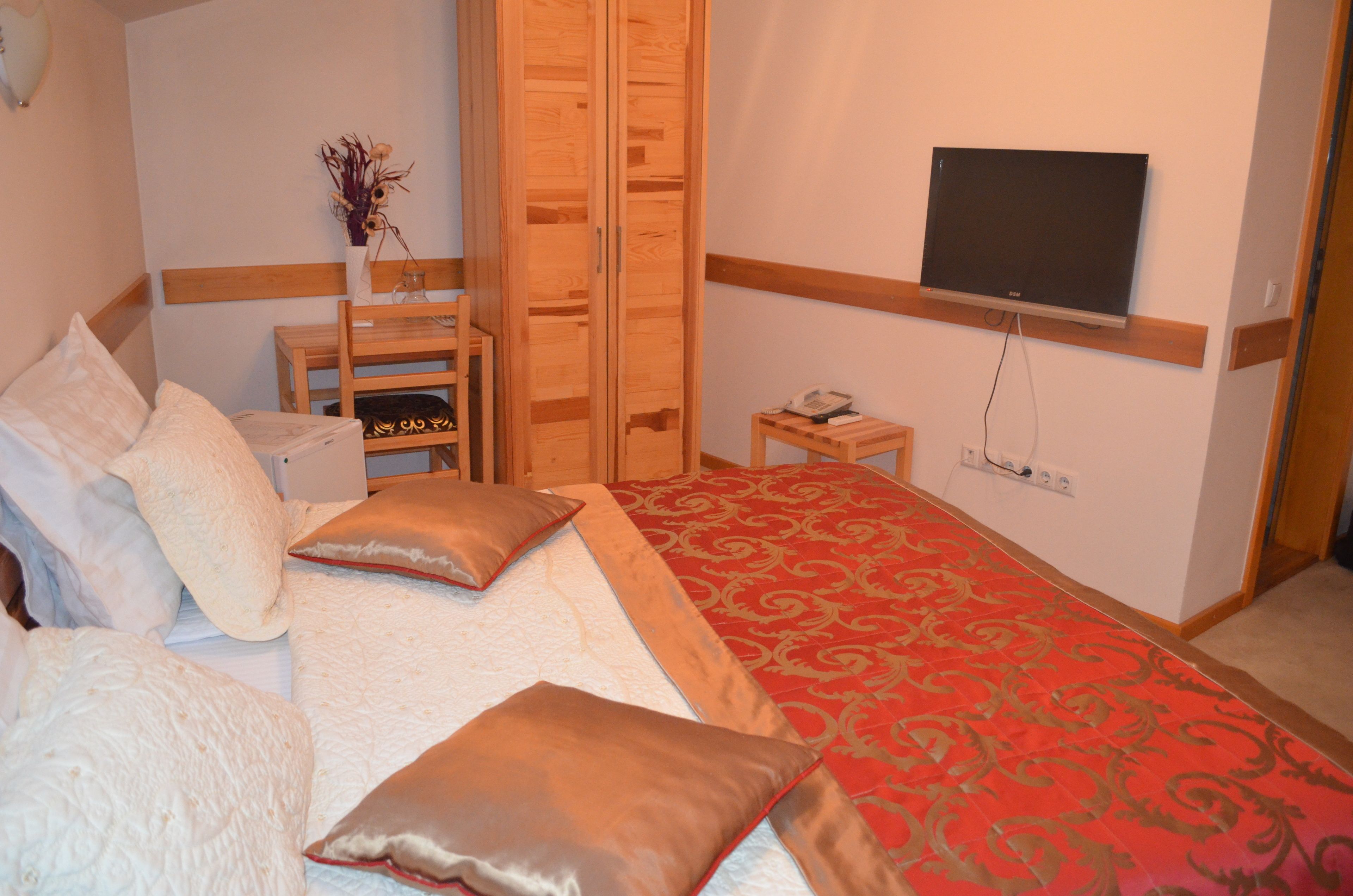 Une chambre à coucher comprenant un lit, une armoire en bois, une petite table avec un vase et un téléviseur fixé au mur.