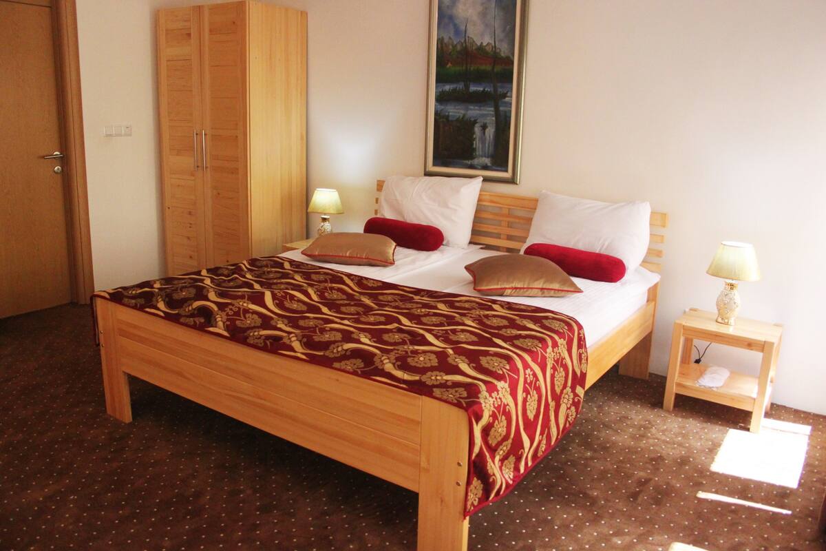 A wooden bed with a patterned bedspread, two bedside tables with lamps, and a painting on the wall.