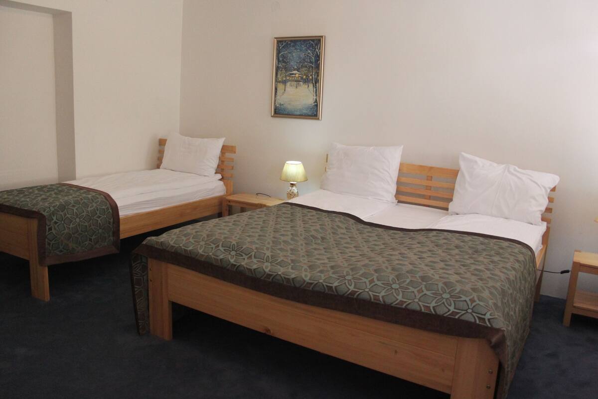 A hotel room with two single beds, a large bed, a nightstand with a lamp, and a painting on the wall.