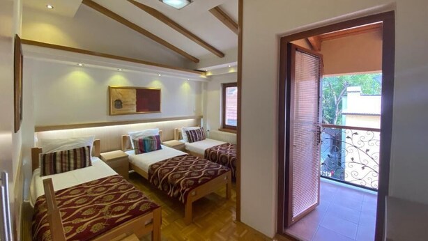 Une chambre avec deux lits simples, un canapé, une petite table et un balcon doté d’une rambarde en métal.