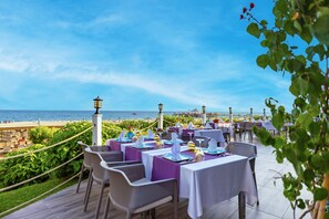 An outdoor dining area with tables set for guests, overlooking a beach and the sea. - VONRESORT Golden Coast - All Inclusive (Manavgat)