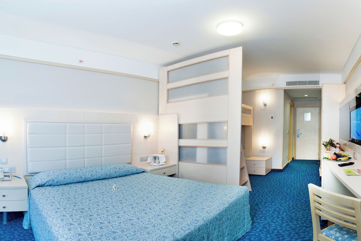 A hotel room with a bed, bedside table, lamp, and a desk with a chair.