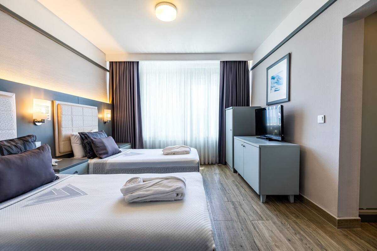 A hotel room with two beds, a television, a desk, and a window with curtains.