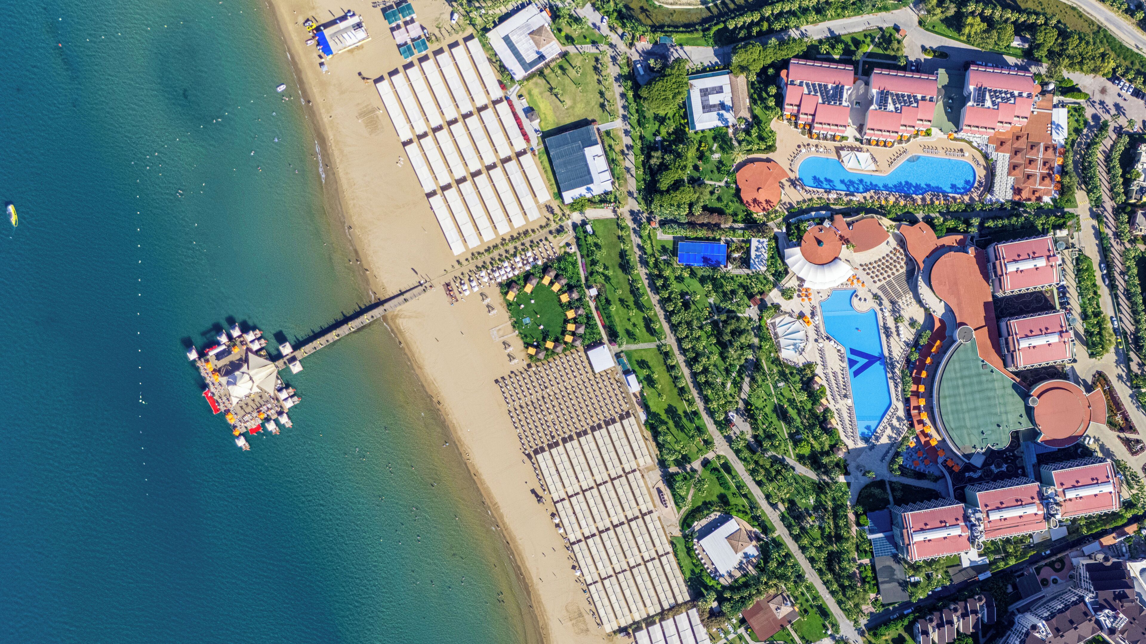 Vista aérea de un resort con playa, un muelle y varias edificaciones con techos rojos.