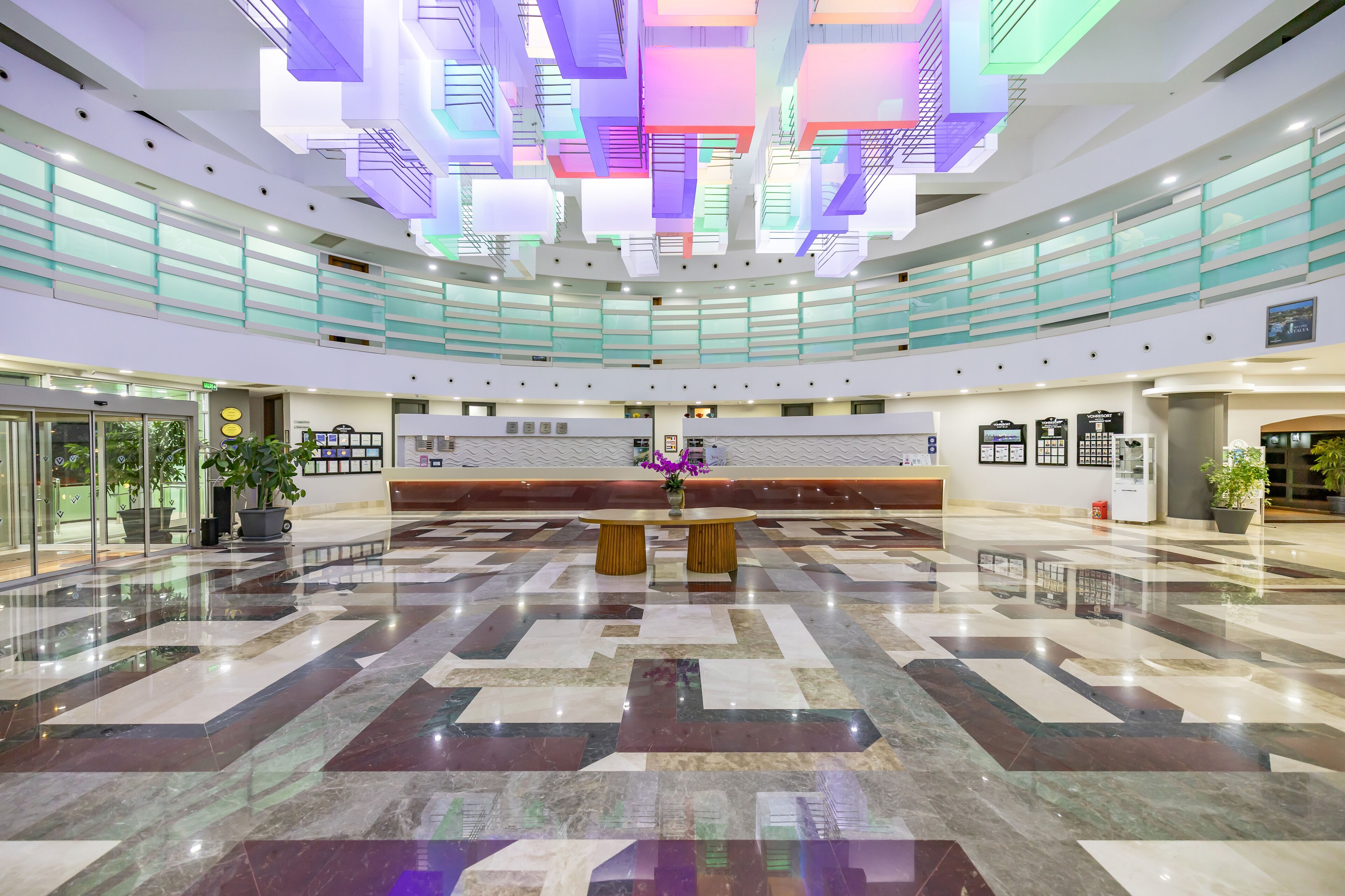 A spacious lobby with a central reception desk, multiple floors, and a modern ceiling design.