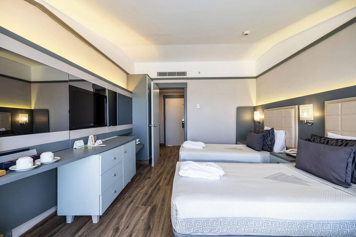 A modern hotel room with a large bed, a bedside table, a built-in TV, and a bathroom with a mirror and sink.