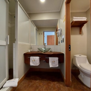 A bathroom with a wooden vanity, a glass sink, and a white toilet. - Hotel Lodge Las Cascadas (Puerto Octay)