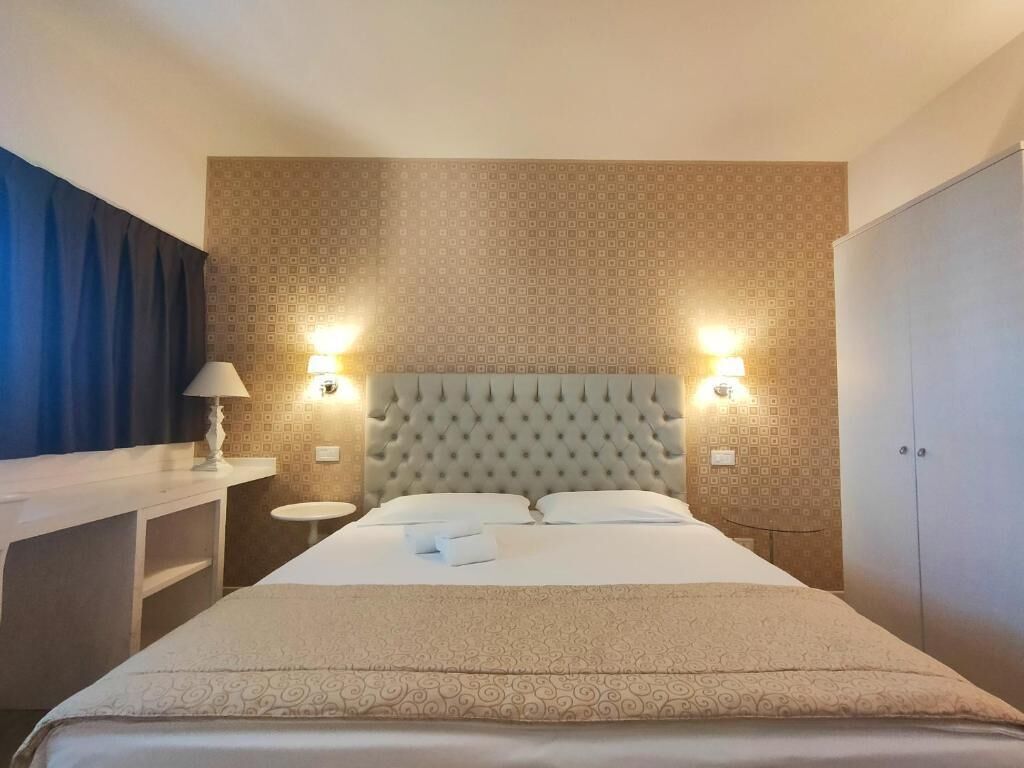 A hotel room with a large bed, two bedside lamps, a round table, and a wardrobe.
