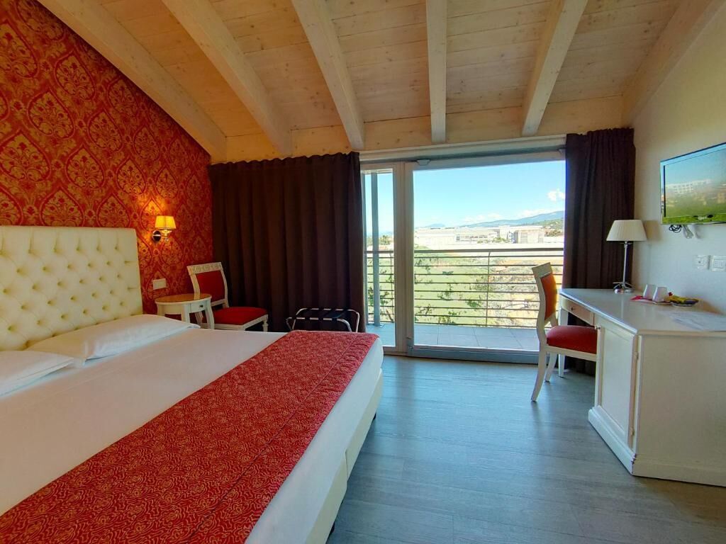 A hotel room with a large bed, a desk, a chair, and a balcony with a view.