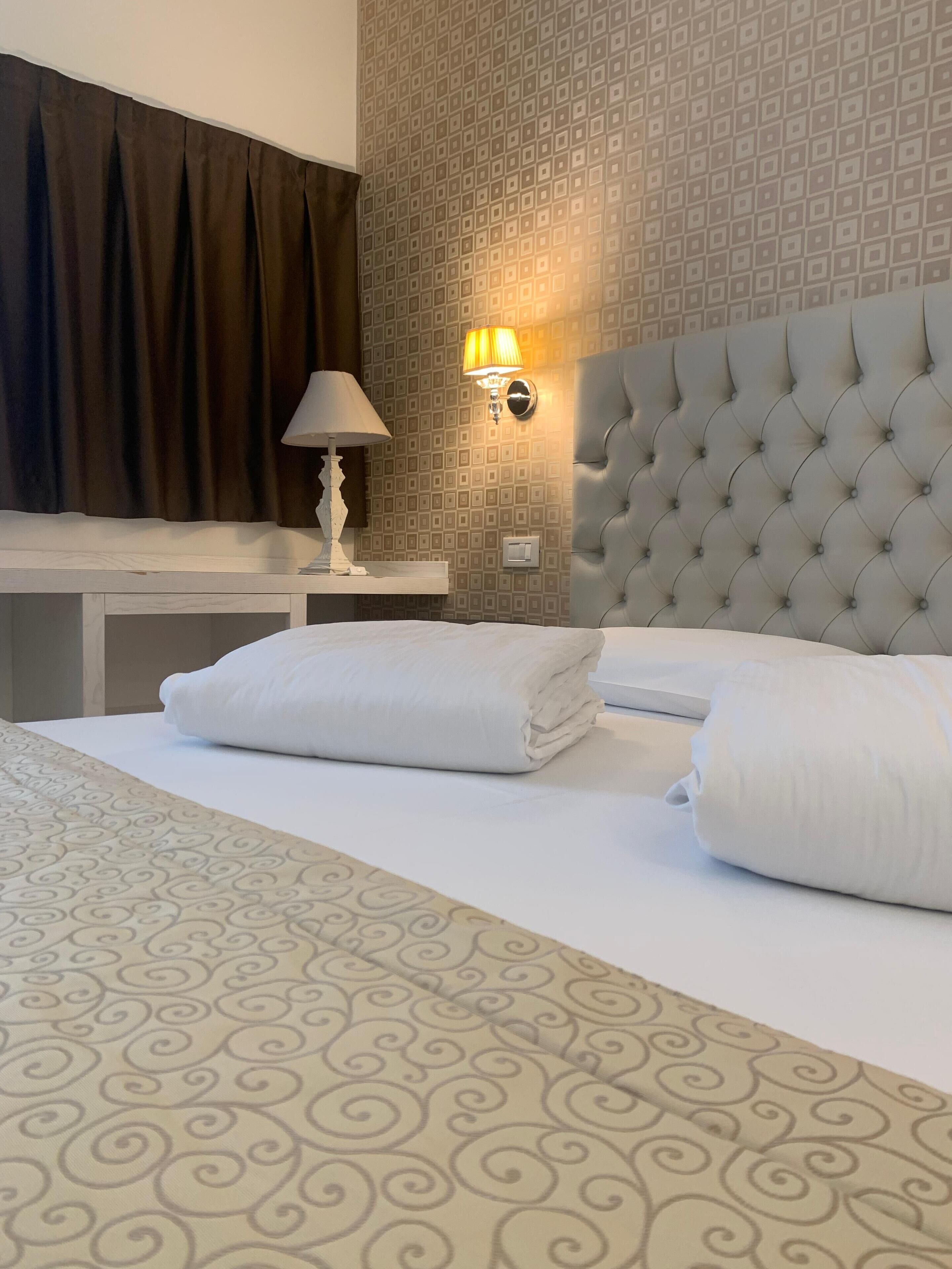 Une chambre d’hôtel avec un lit bien fait, une table de chevet avec une lampe et un mur orné d’un motif géométrique.