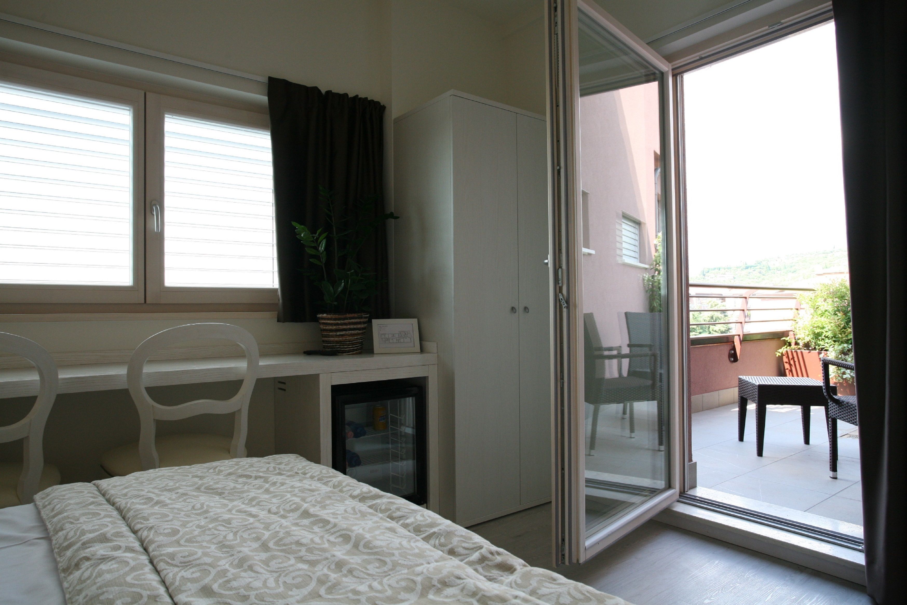 A bedroom with a bed, a desk, a chair, a wardrobe, and a sliding glass door leading to an outdoor patio area.