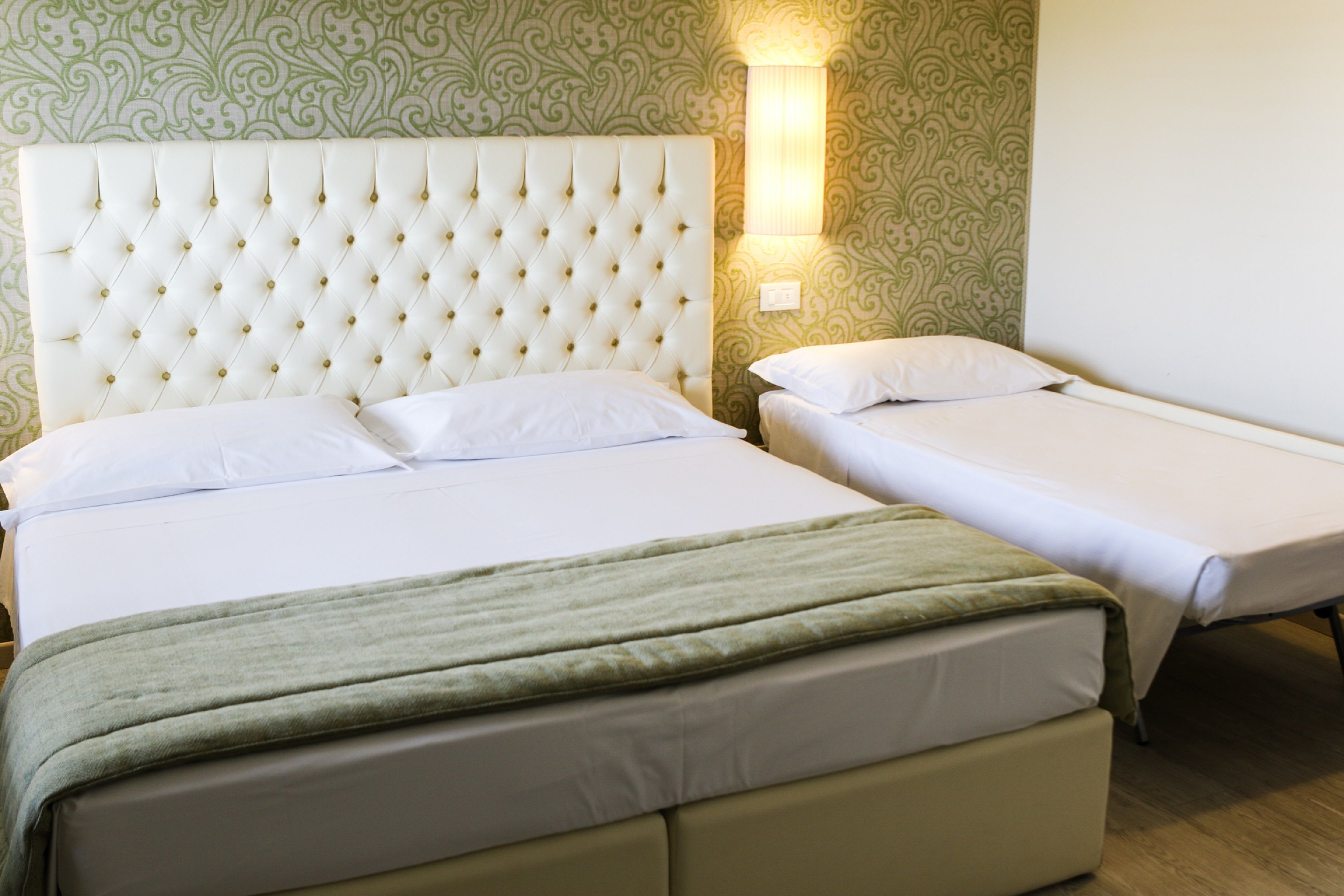 A hotel room with a large bed, a smaller bed, and a nightstand with a lamp.