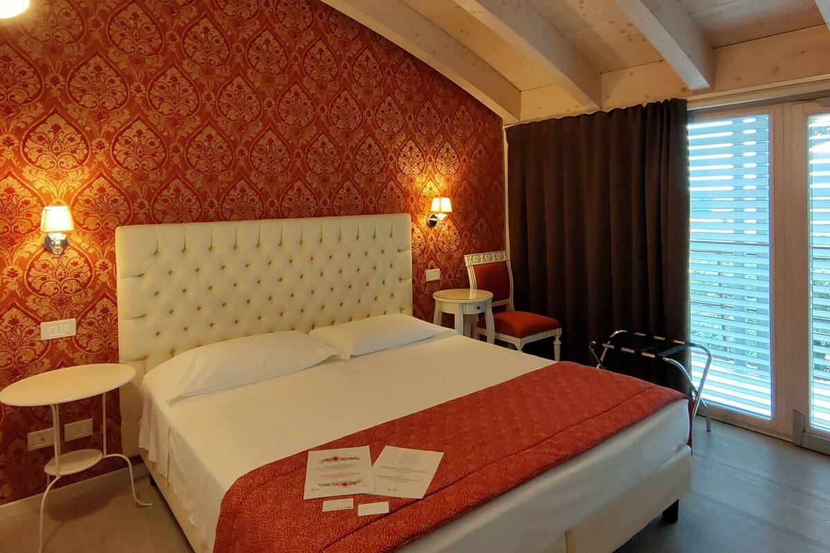 Habitación de hotel con una cama grande, dos mesitas de noche, una mesa pequeña, una silla y una ventana con cortinas.
