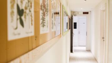 A hallway with framed botanical prints on the wall, a door with a sign, and a light-colored floor.