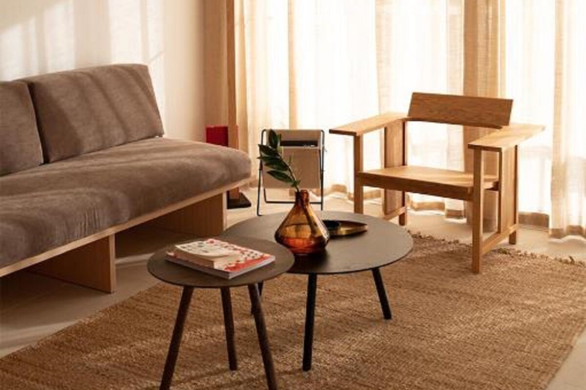 A modern living room with a sofa, a coffee table, and a chair. There is a painting on the wall and a window with curtains.