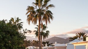 A resort with white buildings, palm trees, and a mountain in the background. - Barcarola Club (Tías)