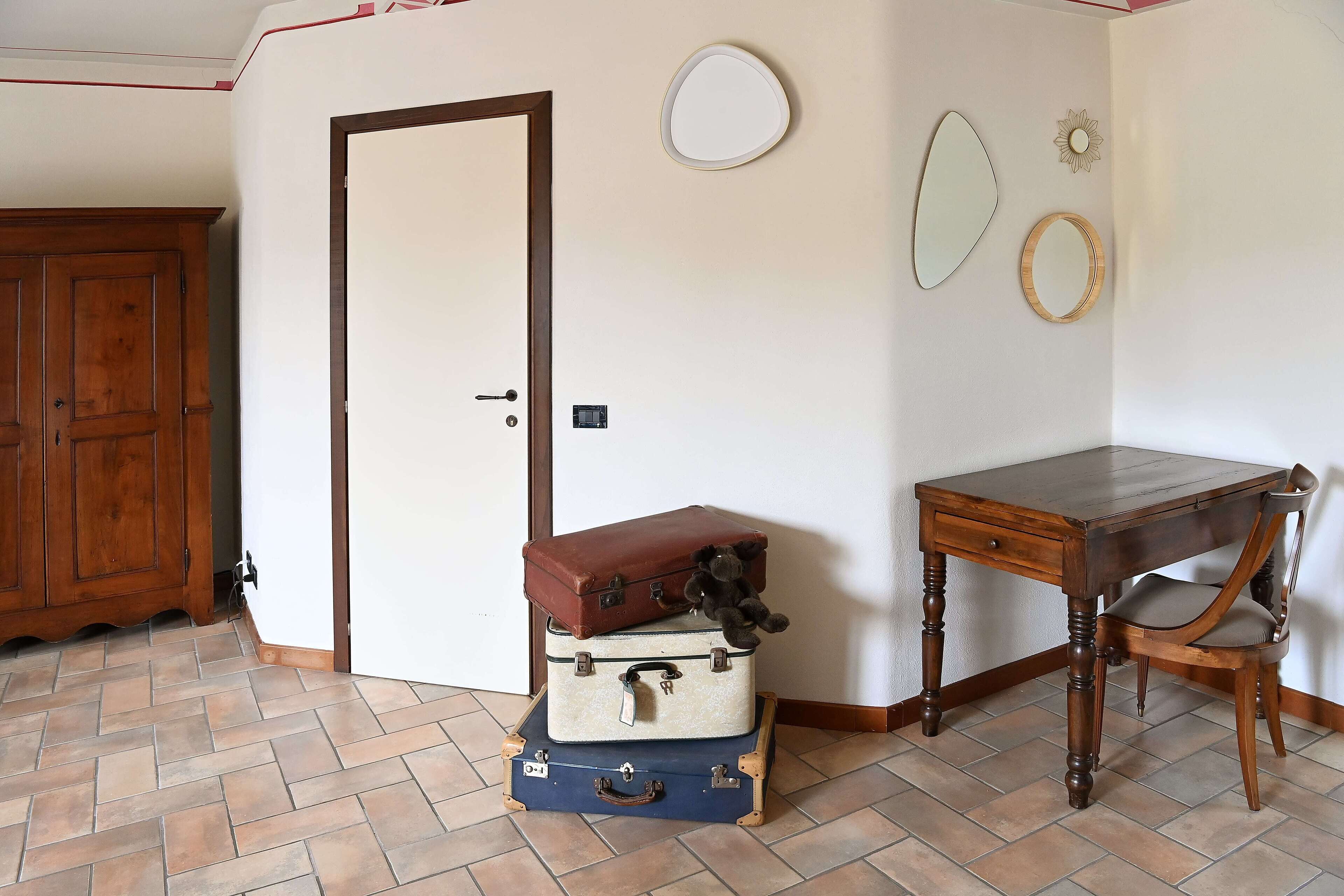 Habitación de esquina con un escritorio de madera, una silla y tres maletas apiladas.