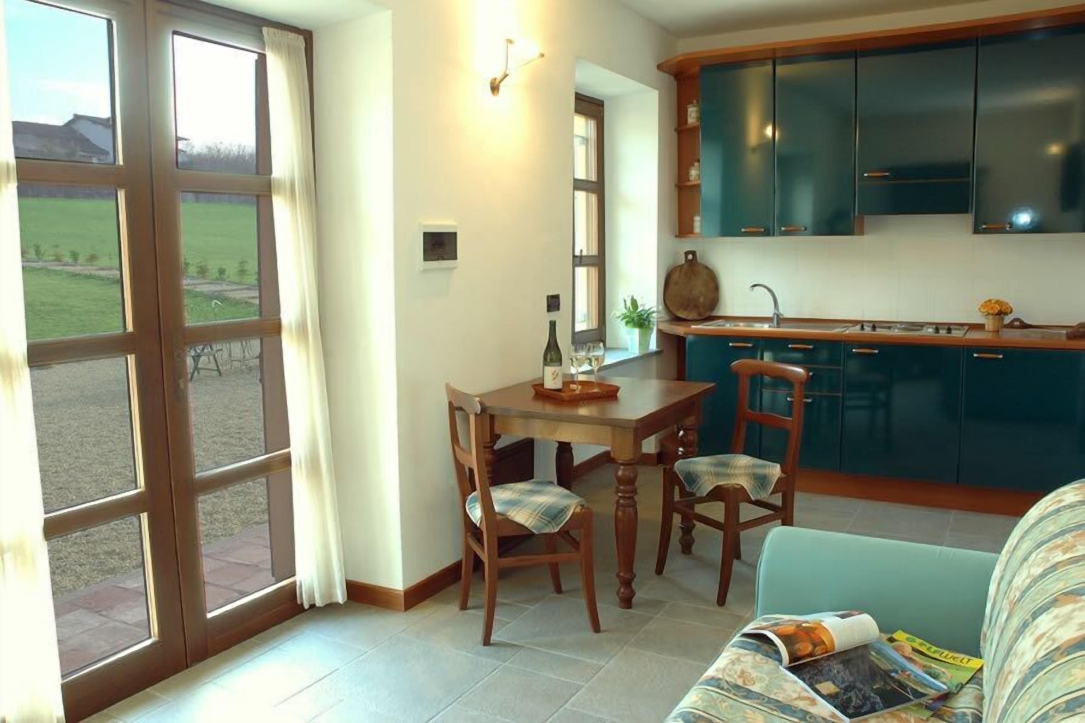 Eine Küche mit Esstisch und Stühlen, ein Fenster mit Vorhängen und Blick auf eine grüne Landschaft.