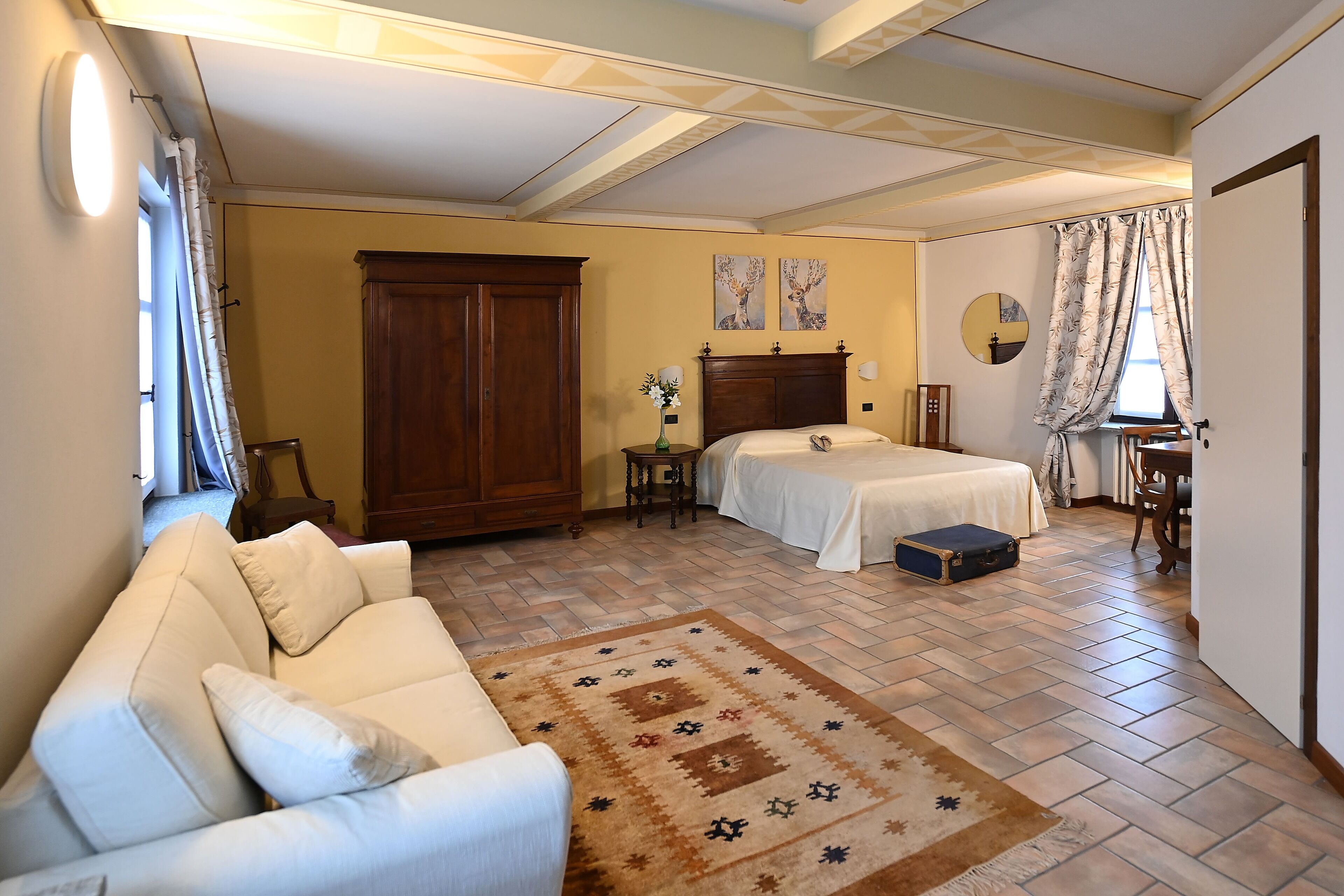 Une chambre à coucher avec un lit double, un canapé, une armoire en bois, une petite table avec un vase et un miroir au mur.