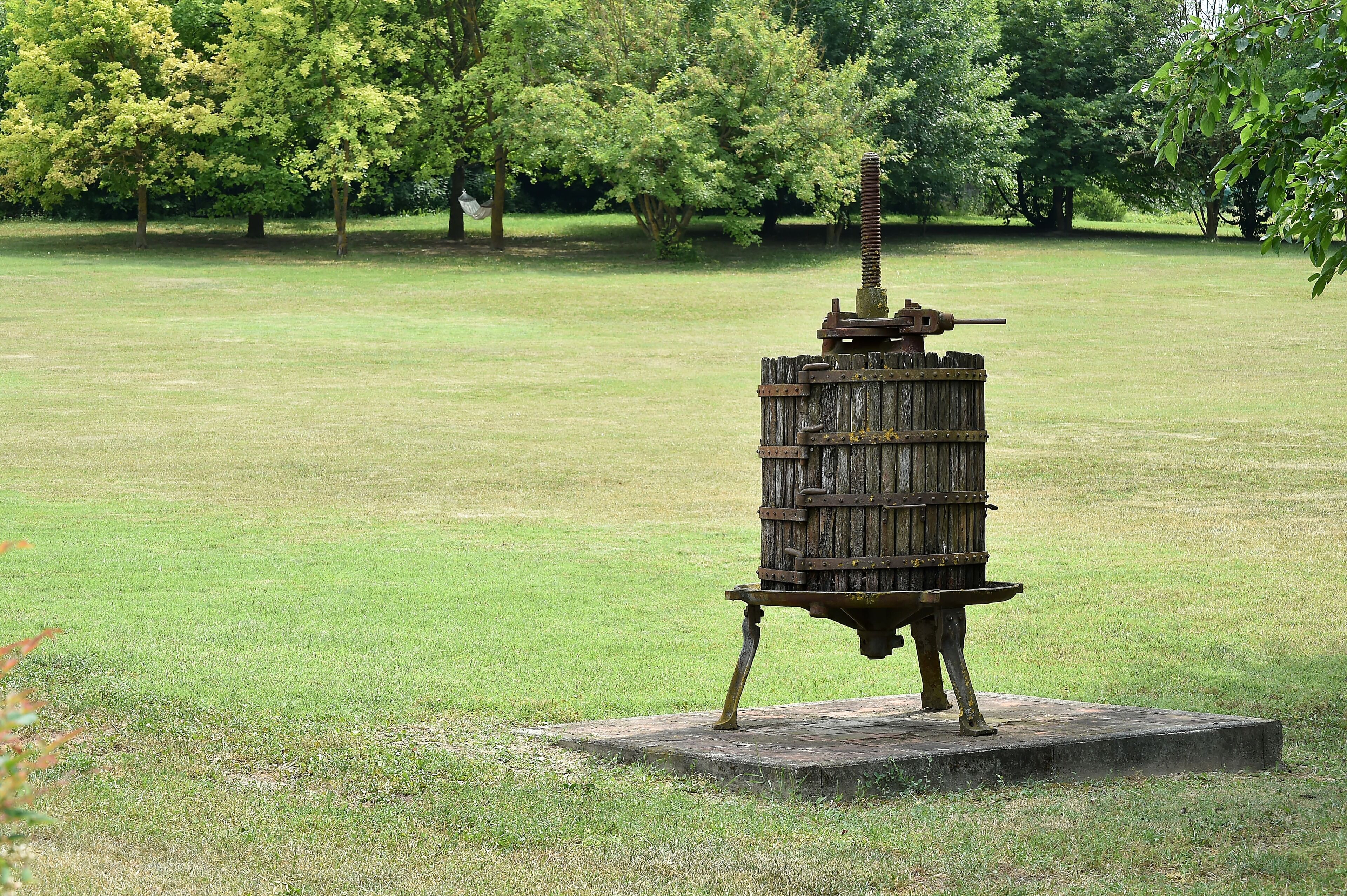 A rustic wooden structure with a metal top, standing on a concrete base in a grassy field.