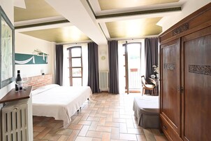 Habitación de hotel con cama, armario de madera, radiador, una mesa con una botella y vasos, y vistas a través de una ventana con cortinas.