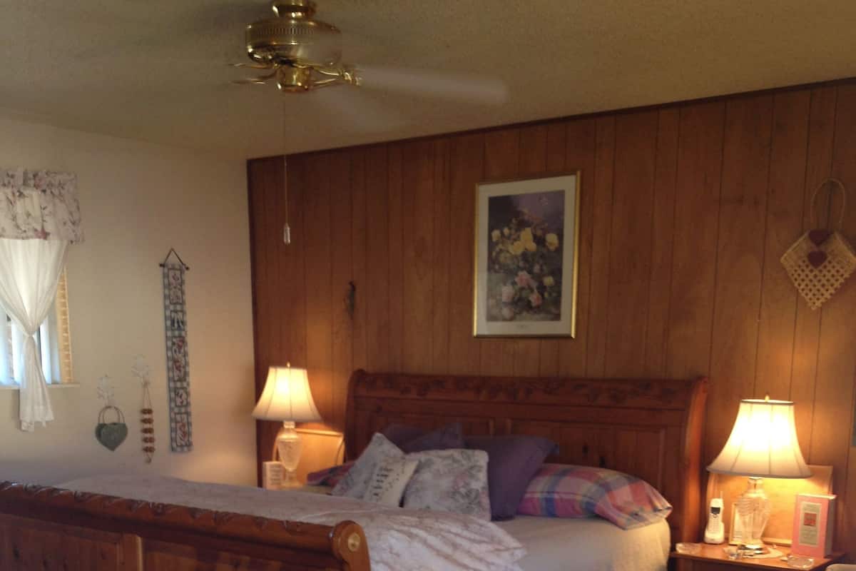 Ein Schlafzimmer mit einem hölzernen Bett, zwei Nachttischen mit Lampen, einem Sessel und einem Deckenventilator.