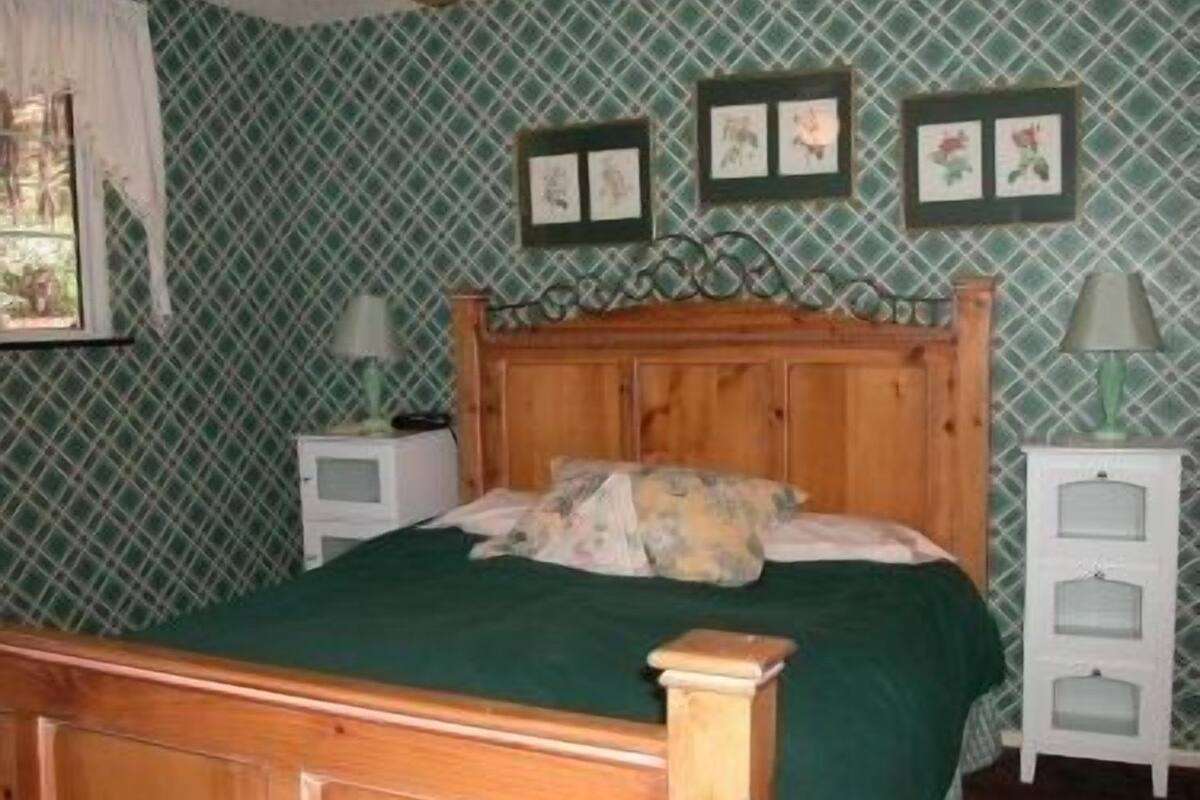 Ein Zimmer mit einem hölzernen Bett, Wandtapete mit grünem Muster und gerahmten Bildern an der Wand.