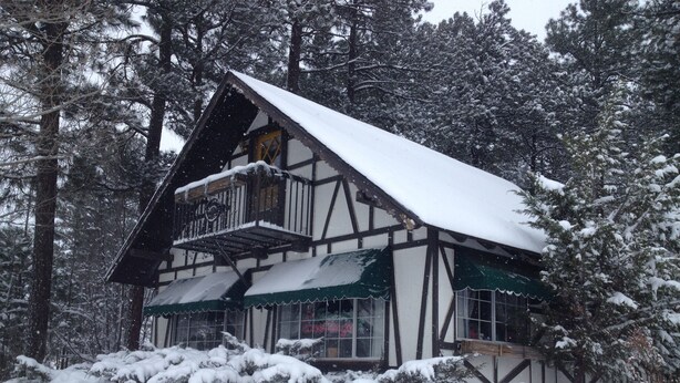 Un chalet traditionnel à ossature en bois, doté d’un balcon et entouré d’arbres couverts de neige.
