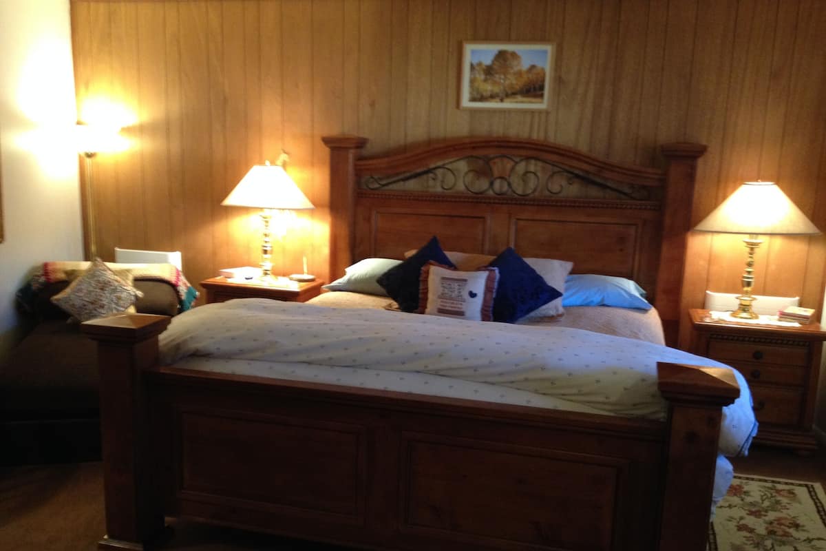 Ein hölzernes Himmelbett mit Kopfteil, begleitet von zwei Nachttischen mit Lampen, einem Teppich mit floralem Muster und einem gerahmten Bild an der Wand.