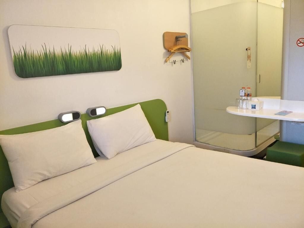 Una camera d'albergo con un letto, un comodino con articoli da toilette, uno specchio e un porta asciugamani a parete.