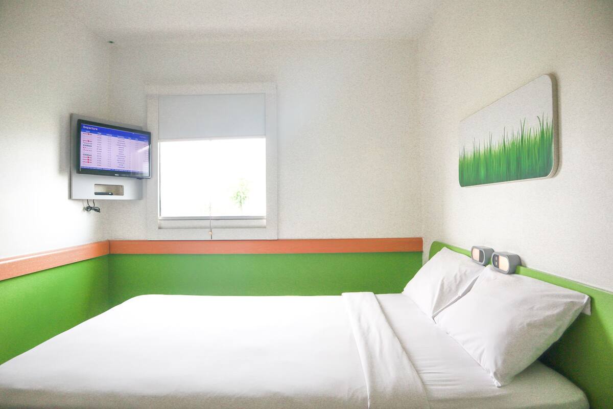 Ein Hotelzimmer mit einem Bett, einem an der Wand montierten Fernseher, einem Fenster und einer Wandgestaltung in Grün und Weiß.
