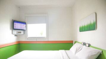 Habitación de hotel con cama, televisión montada en la pared, ventana y una decoración de paredes en tonos verde y blanco.