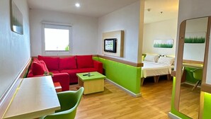 A modern living room with a red sofa, green chairs, a wooden coffee table, and a TV mounted on the wall.