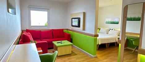 A modern living room with a red sofa, green chairs, a wooden coffee table, and a TV mounted on the wall.
