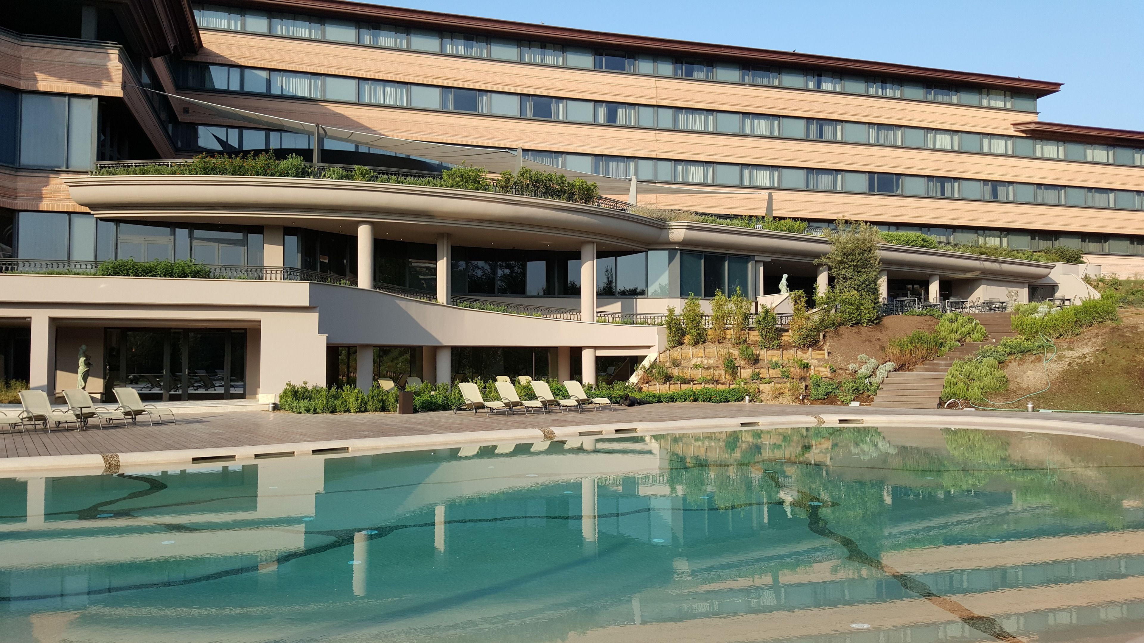 Un hotel moderno con una piscina amplia, varios balcones y un jardín ajardinado.
