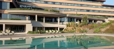 Un hotel moderno con una piscina amplia, varios balcones y un jardín ajardinado.