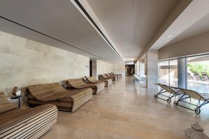 A spacious lobby with a row of wooden benches and a row of sun loungers.
