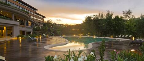 A pool area with a curved design, surrounded by lounge chairs and a building with multiple floors and balconies.