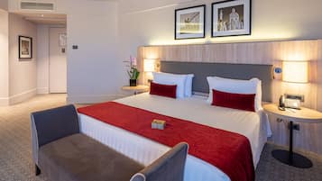 Quarto de hotel com uma cama grande, duas mesas de cabeceira, uma cadeira e uma mesinha com abajur.