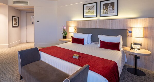Une chambre d’hôtel avec un grand lit, deux tables de chevet, une chaise et une petite table avec une lampe.