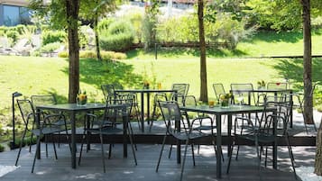 An outdoor patio with metal tables and chairs, surrounded by greenery and trees.
