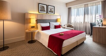 Una camera d'albergo con un letto grande, un comodino, una sedia, una scrivania e una finestra con tende.