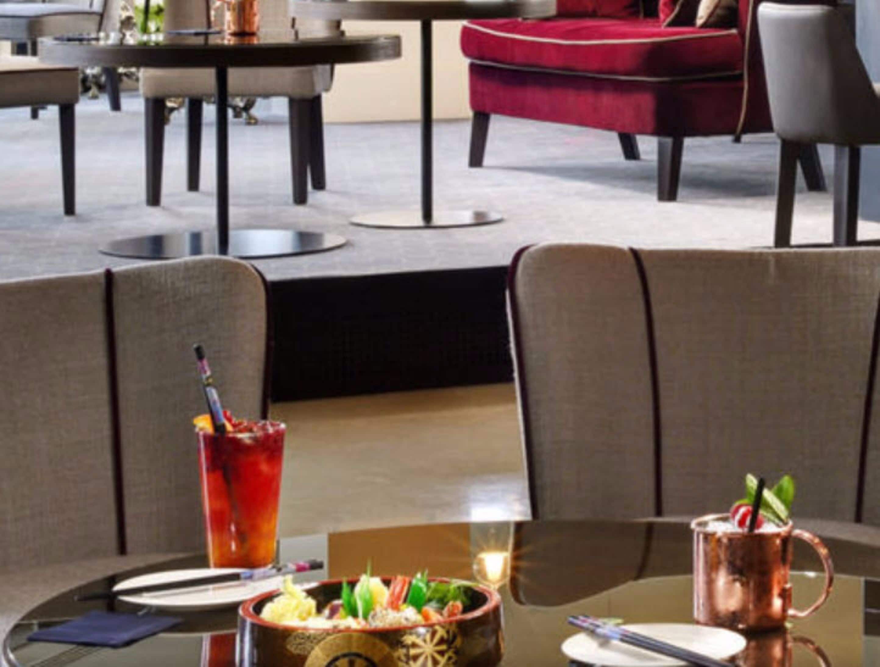 A modern dining area with round tables, cushioned chairs, and a red upholstered chair.